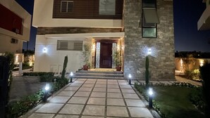 Une maison moderne à deux étages, dotée d’une façade en pierre, d’une entrée centrale avec des marches et d’un éclairage extérieur.
