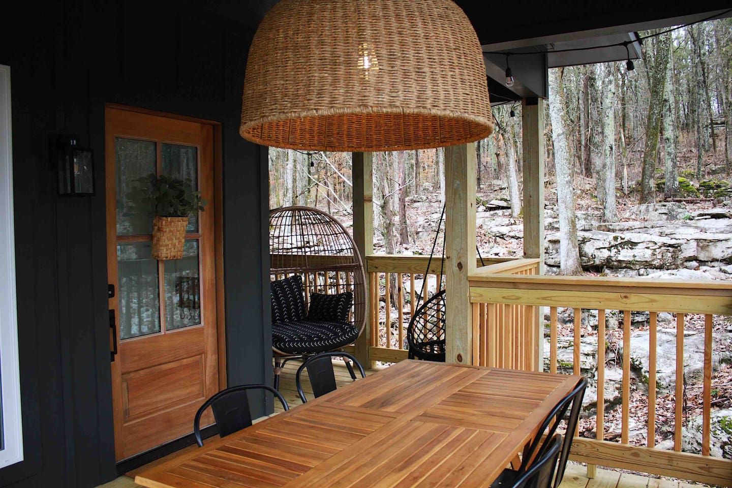 Een houten terras met een eettafel en stoelen, een hanglamp van riet en een rieten stoel met kussens.