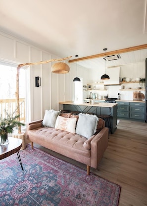 Una sala de estar acogedora con un sofá, un tapete estampado y un comedor con una cocina al fondo.