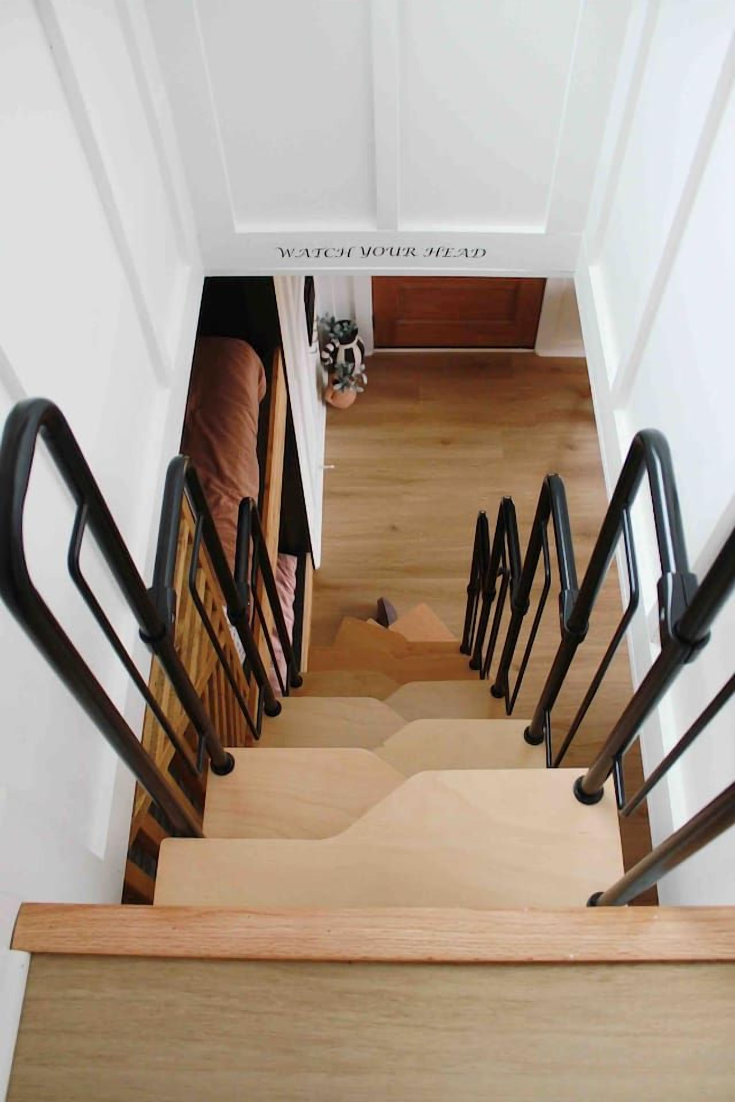 Una scala con gradini in legno e ringhiere nere, che conduce a una stanza con un letto e una porta.