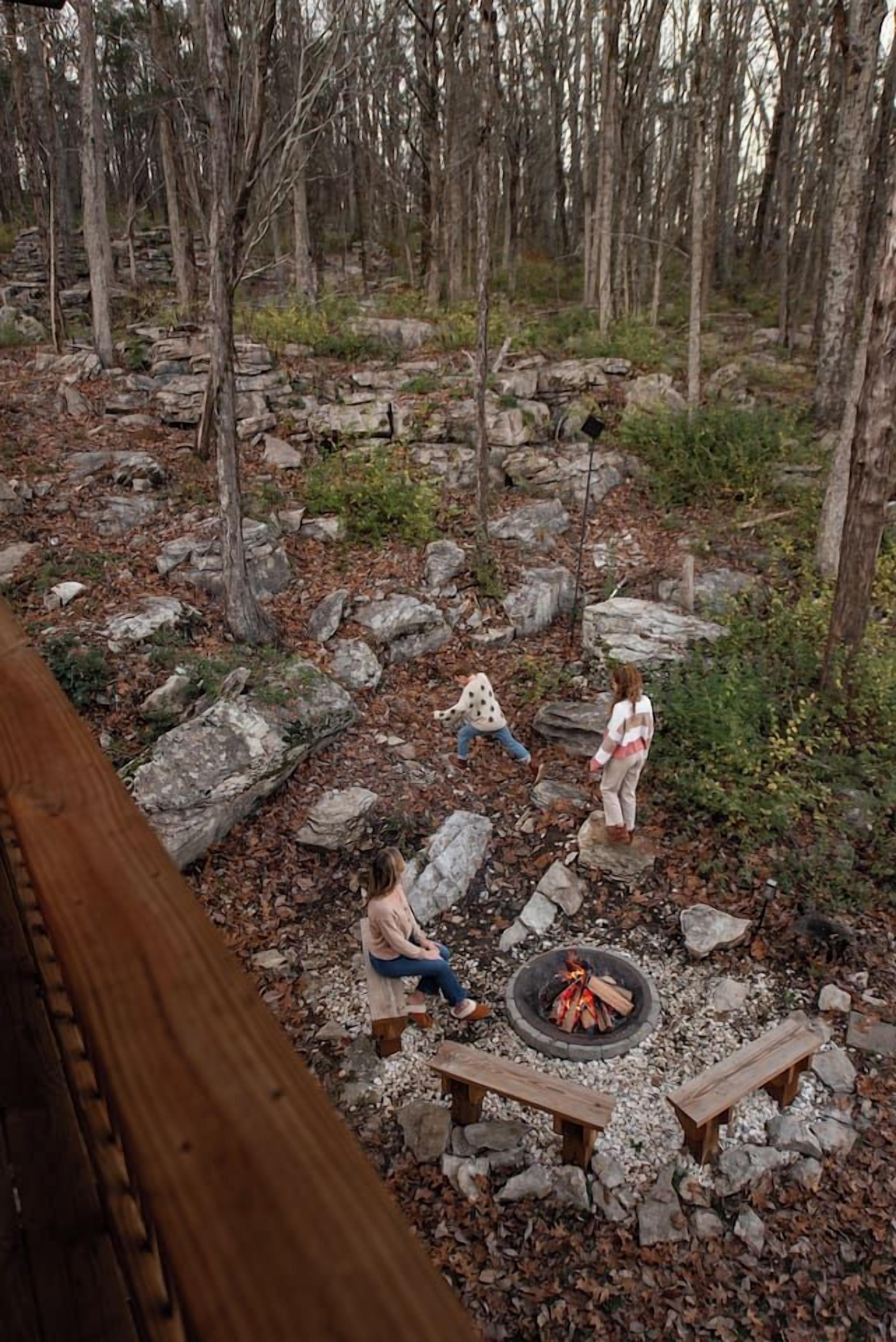 A campsite with a fire pit, wooden benches, and a forested area.