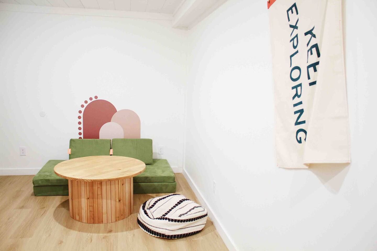 A minimalist room with a round wooden table, green upholstered seating, and a wall-mounted banner.