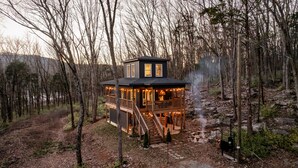 Une cabane dotée d’une terrasse, d’une cheminée et d’un mur en pierre.