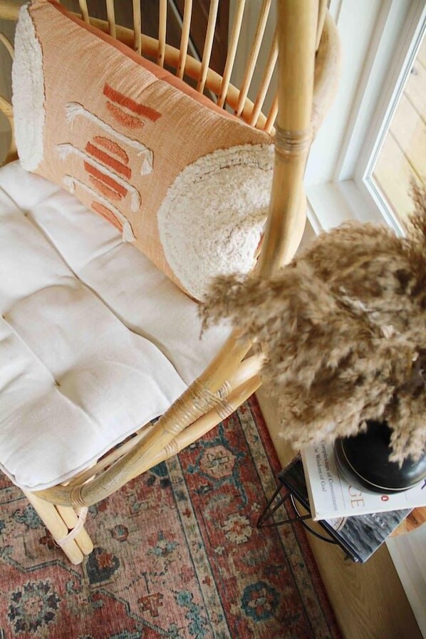 A wicker chair with a cushion, a patterned rug, and a potted plant.