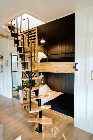 Una habitación compacta con una cama individual superior e inferior, una escalera de madera y una pequeña zona de estar.