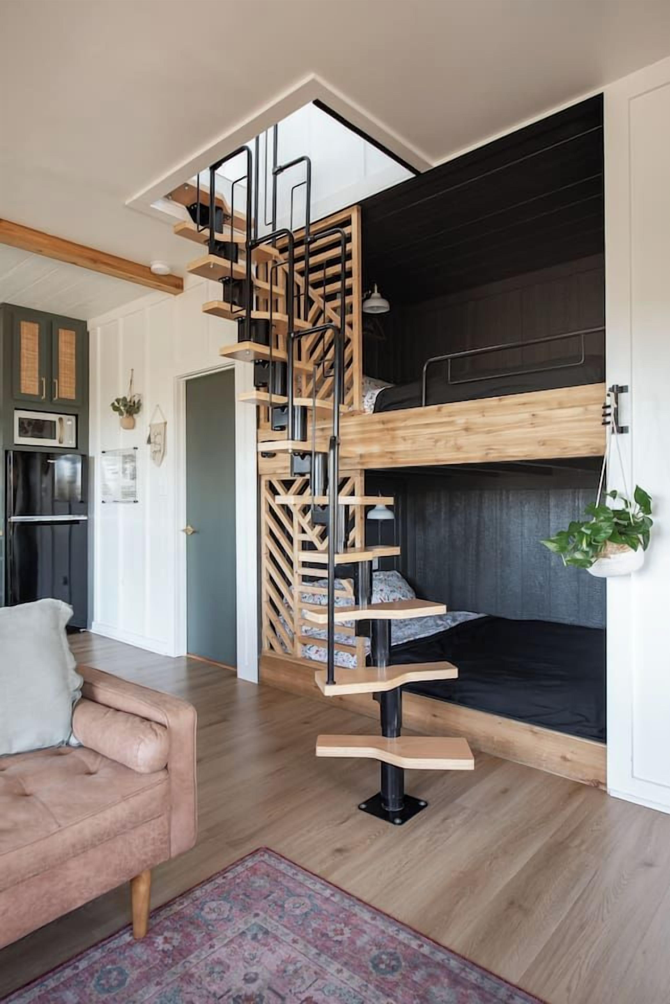 A modern interior with a wooden staircase leading to a bunk bed, a kitchen area, and a seating area with a couch.