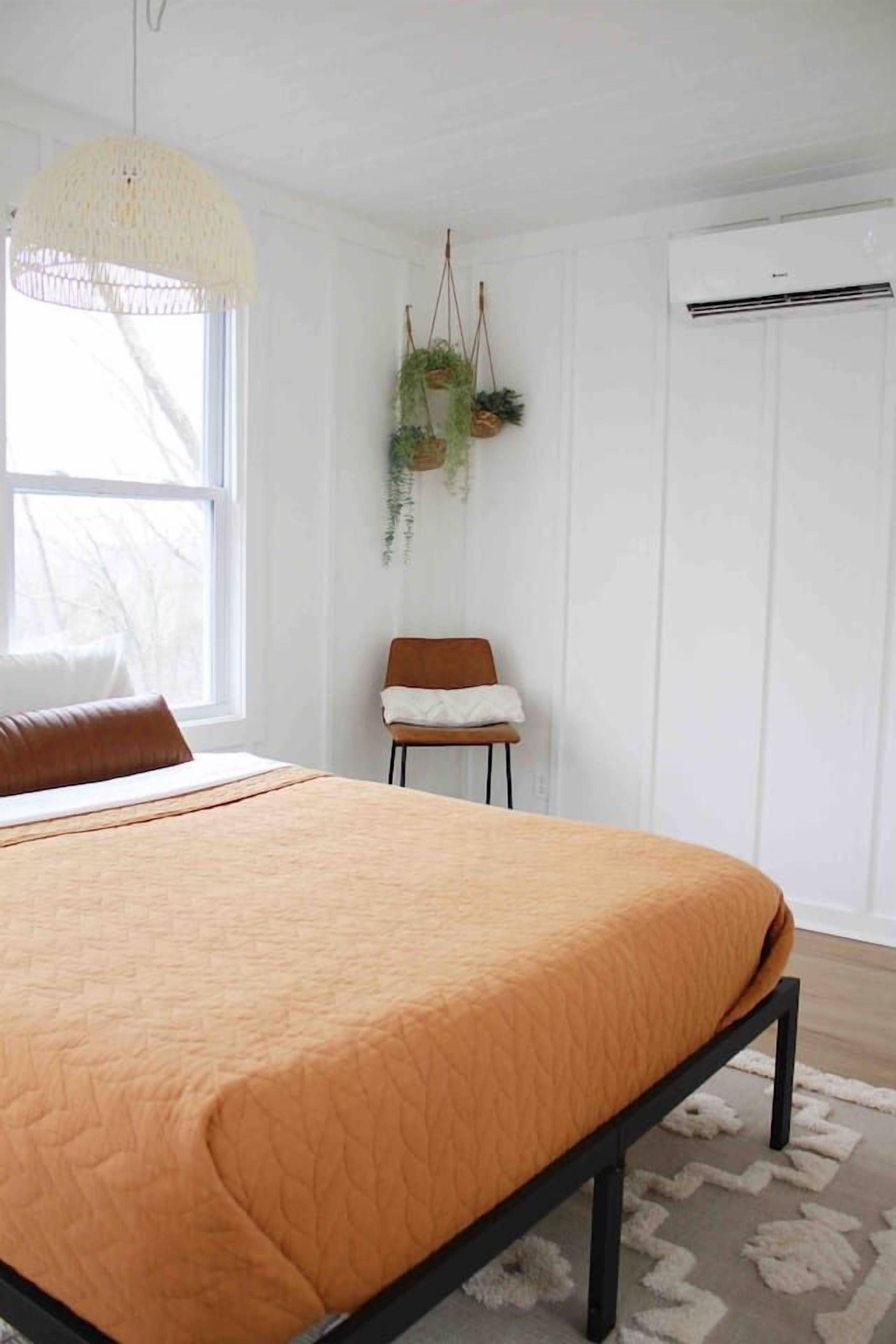 Ein Schlafzimmer mit einem Bett, einer hängenden Pflanze, einem Stuhl und einem Fenster.