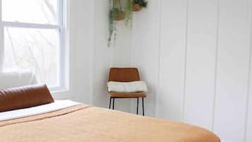 Ein Schlafzimmer mit einem Bett, einer hängenden Pflanze, einem Stuhl und einem Fenster.