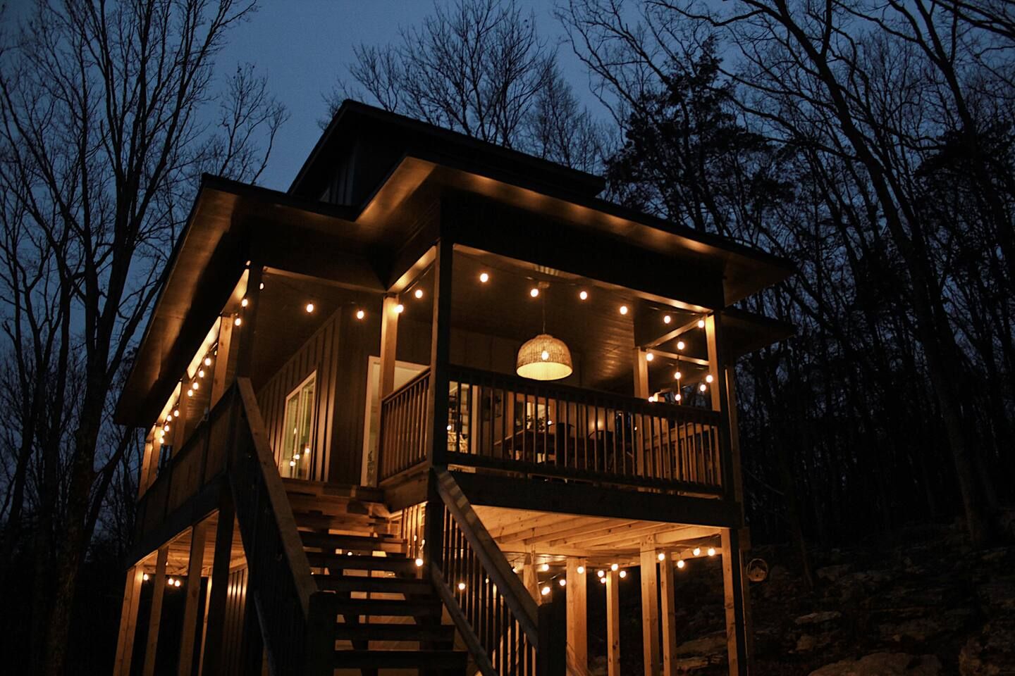 A two-story wooden cabin with a balcony, surrounded by trees.