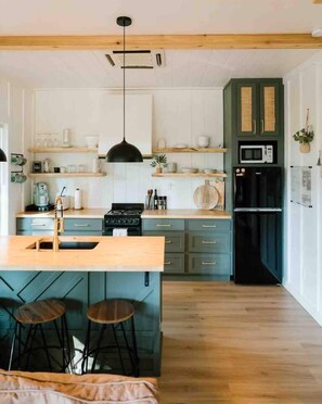 Una cocina moderna con una isla central, taburetes de bar, microondas y refrigerador.