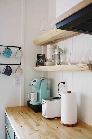 A kitchen with a wooden countertop, a coffee maker, a toaster, and a hanging mug rack.