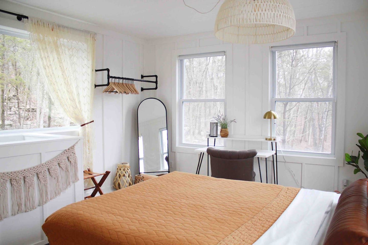Een slaapkamer met een bed, een bureau, een stoel, een spiegel en twee ramen.