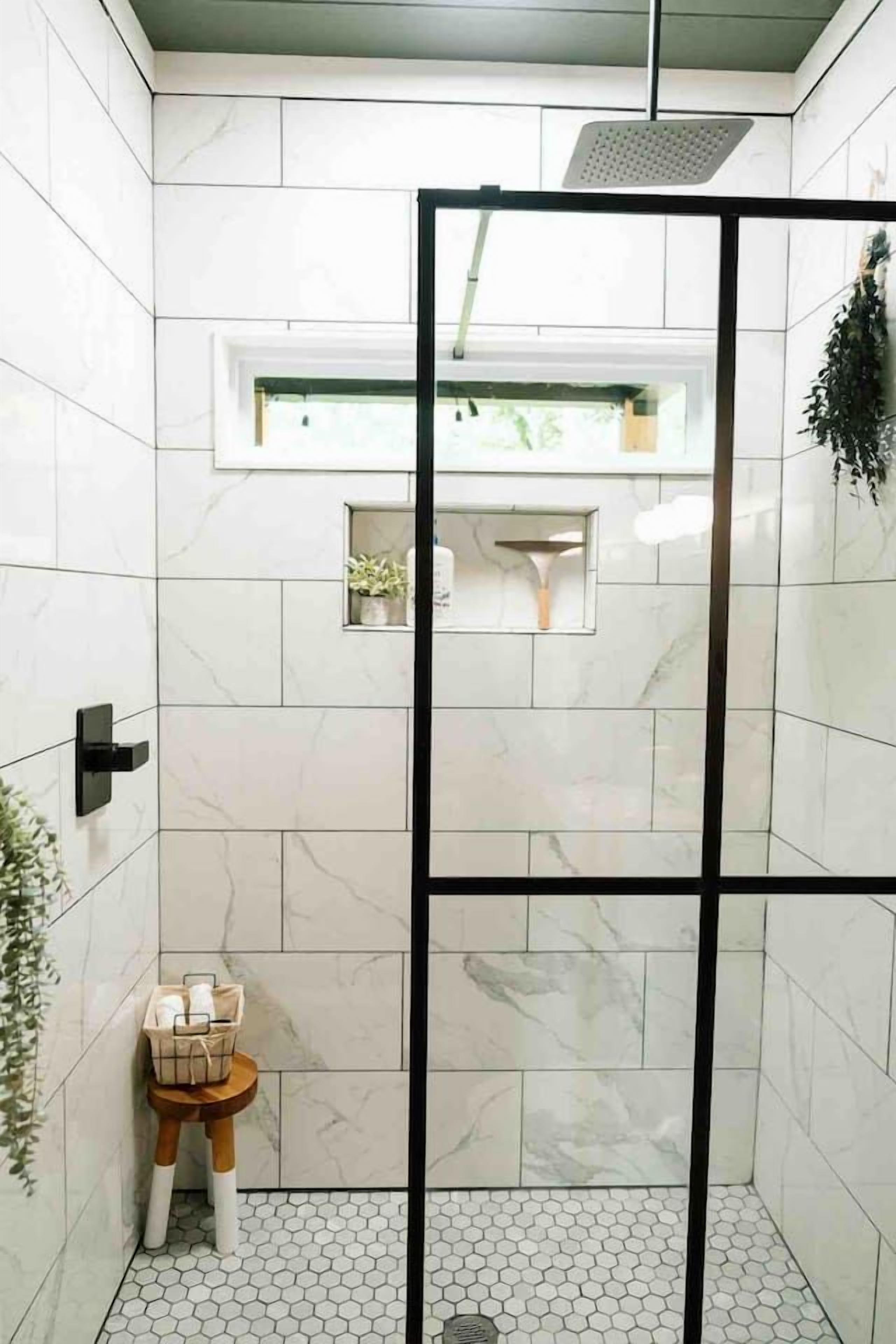 A bathroom with white marble tiles, a shower enclosure, a small sink, and a plant.