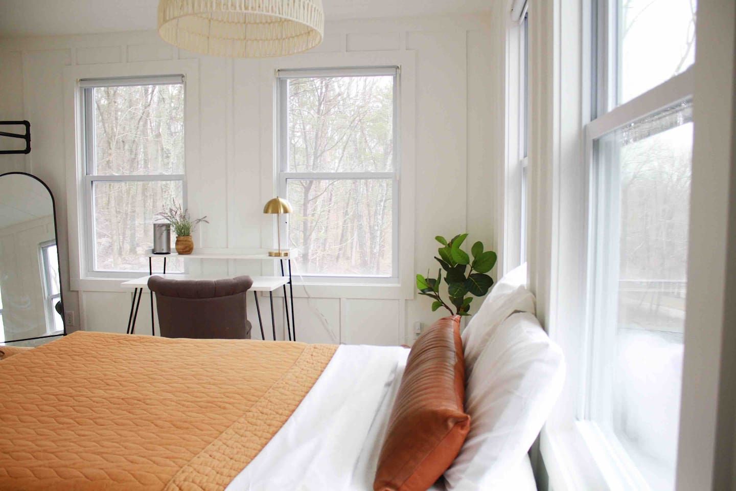 Un dormitorio con una cama grande, dos ventanas, un escritorio con silla y una planta en maceta.