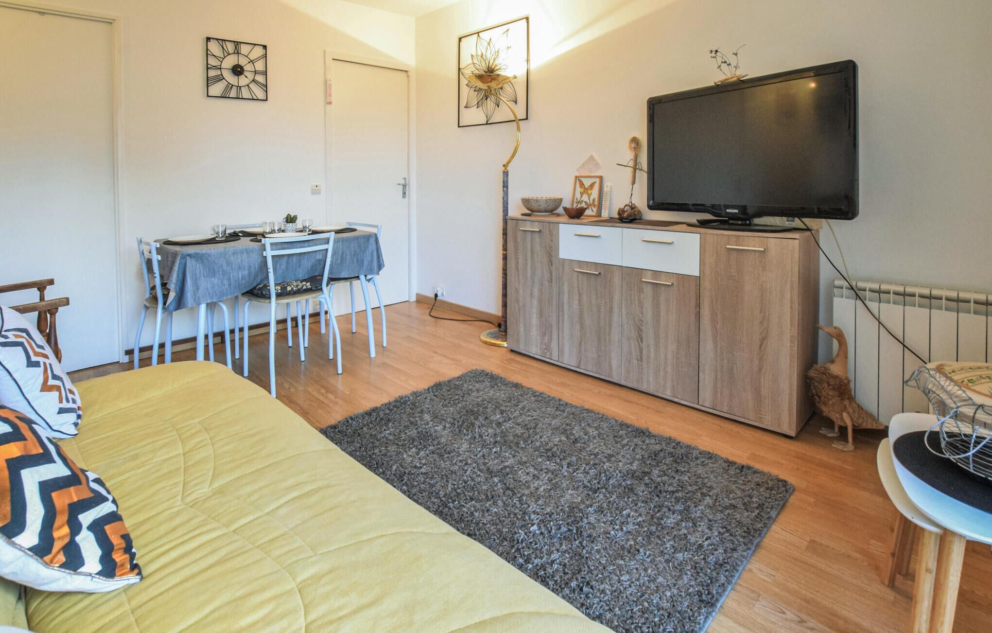 A compact living space with a bed, a dining table with chairs, a TV, and a small cabinet.