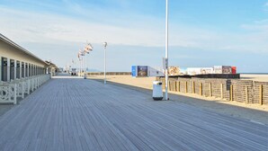 A wooden boardwalk leading to a beach with flags and a lighthouse in the distance. - 1 bedroom gorgeous apartment in Blonville-sur-Mer (Blonville-sur-Mer)