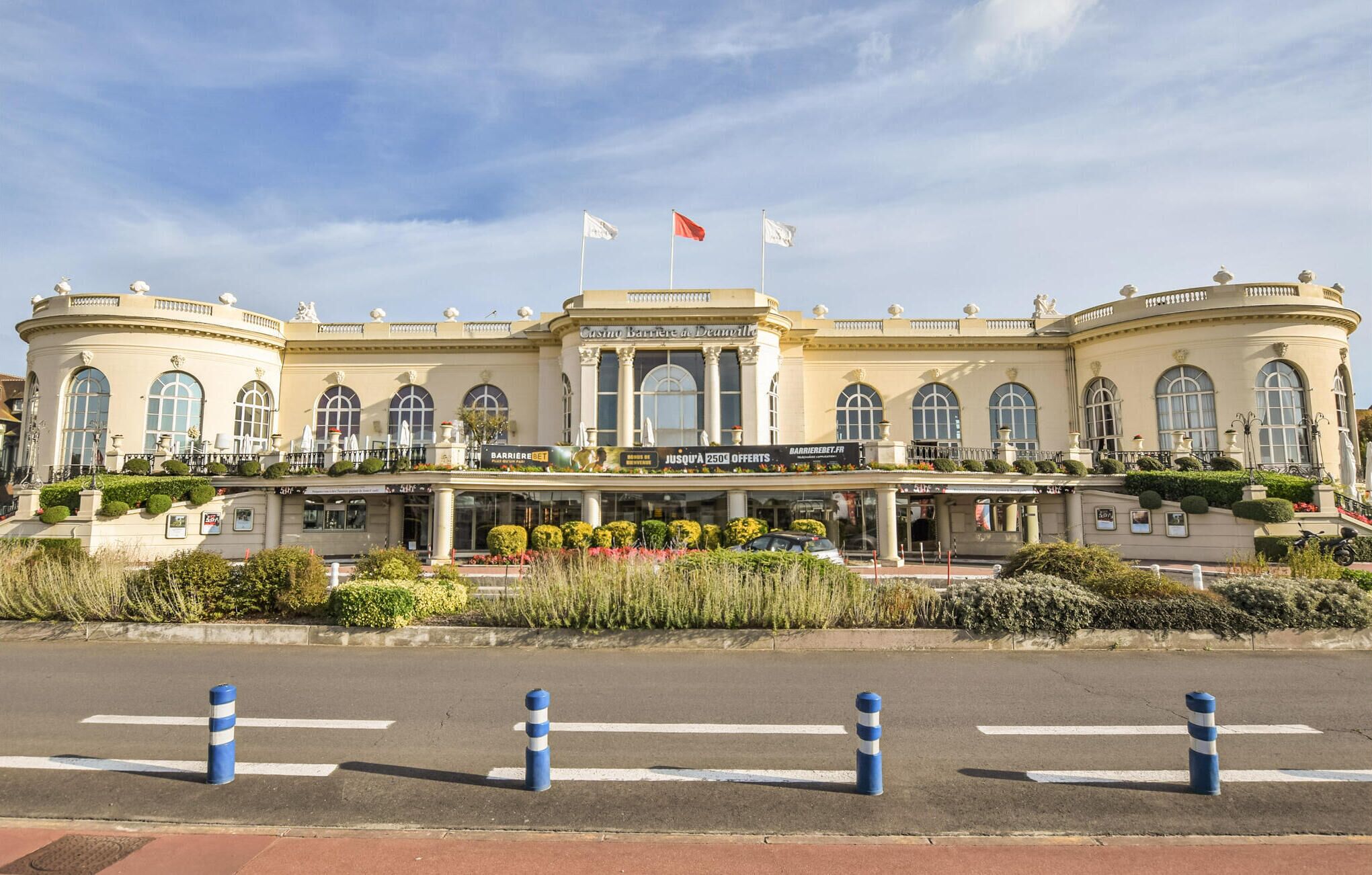 Un edificio grande de estilo clásico, con una entrada central, varias banderas y un jardín delantero.