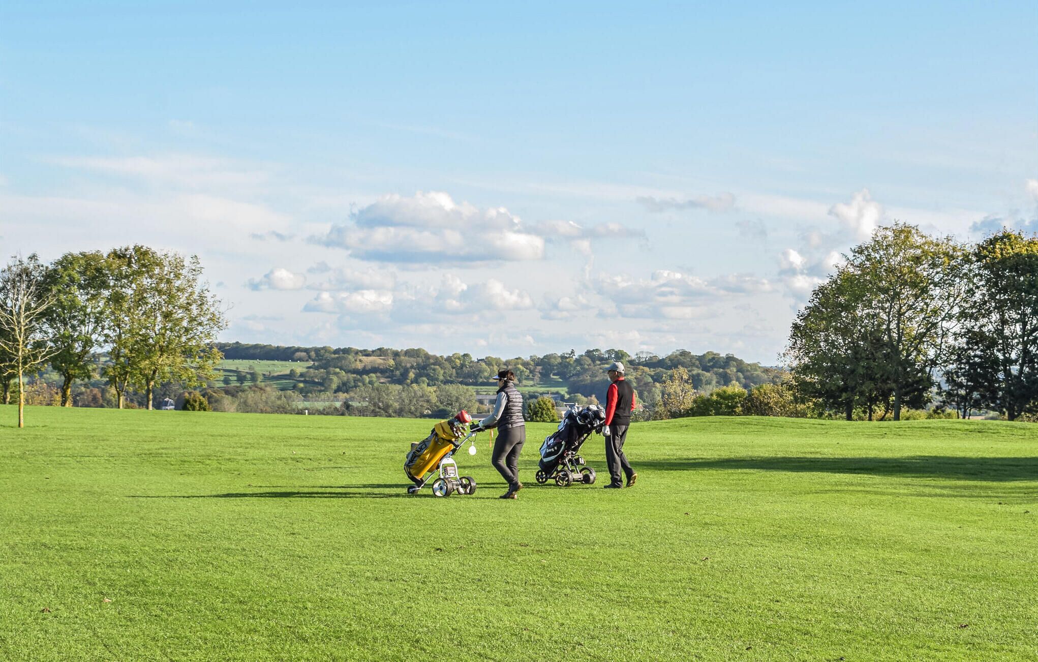 A golf course with a clear sky, trees, and rolling hills in the background.