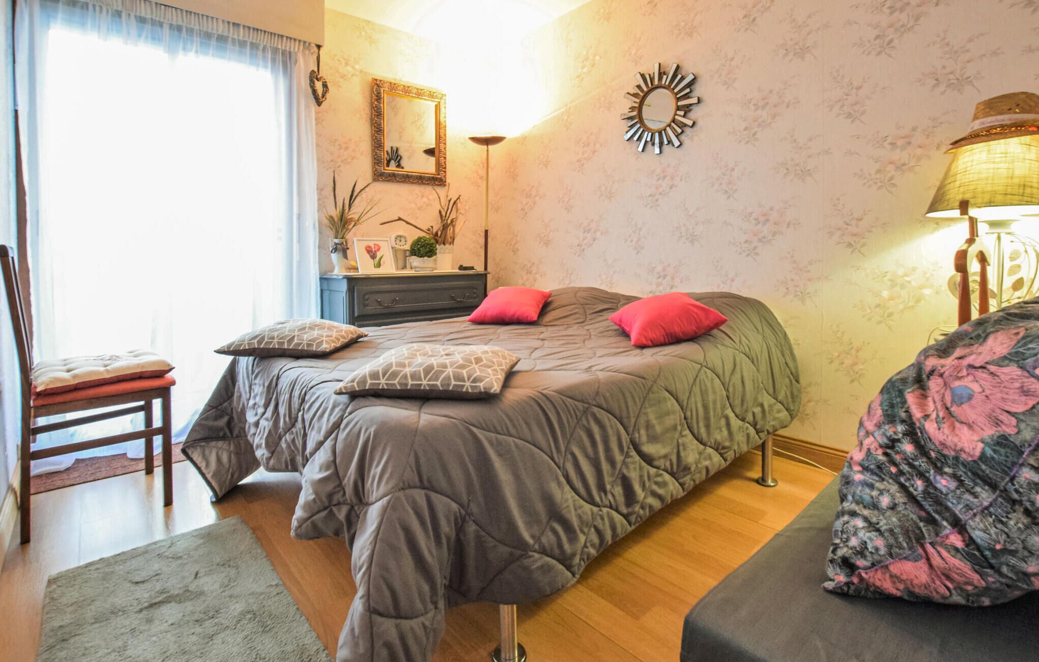 A bedroom with a bed, a chair, a dresser, a mirror, and a lamp.