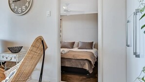 Une pièce comprenant un lit, une chaise en osier, une horloge murale et un ventilateur de plafond.