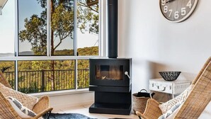 Une pièce chaleureuse avec une grande fenêtre, un poêle à bois noir, des fauteuils en osier et une horloge murale.