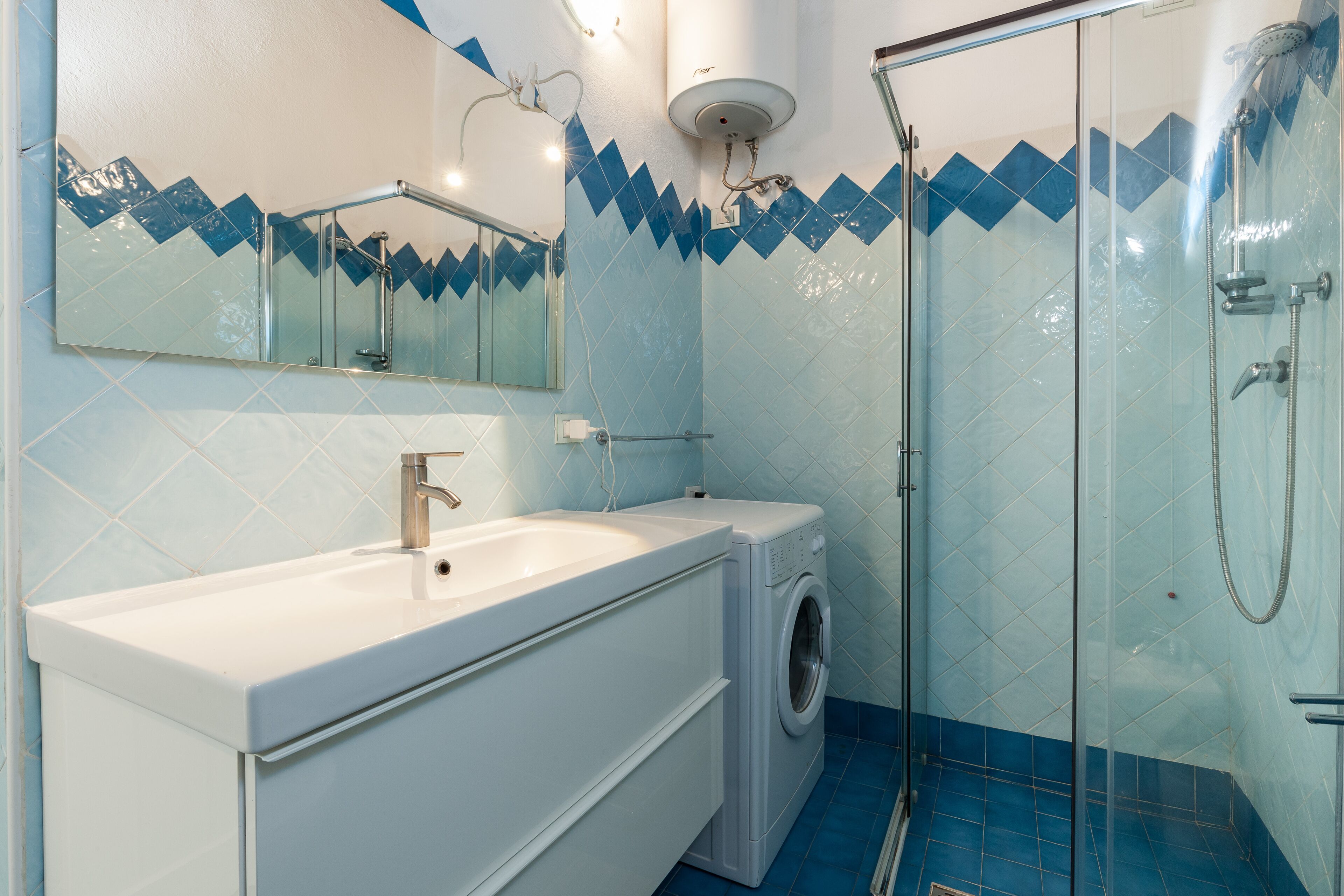 A bathroom with a sink, washing machine, and glass-enclosed shower.