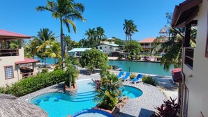 A resort with a swimming pool, palm trees, and a view of the water. - Beautiful Island Townhome Overlooking Caribbean (Placencia Village)