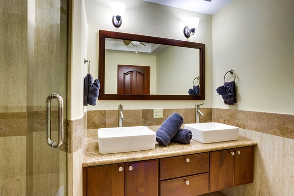Une salle de bain avec un grand miroir, deux lavabos, un porte-serviettes et un espace douche.