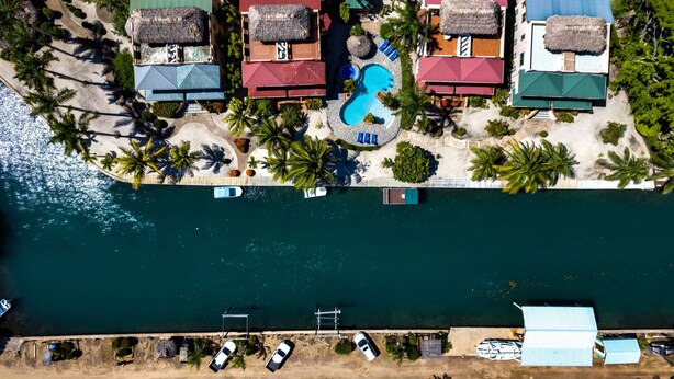 An aerial view of a resort with multiple buildings, a swimming pool, and a dock with boats. - Beautiful Island Townhome Overlooking Caribbean (Placencia Village)