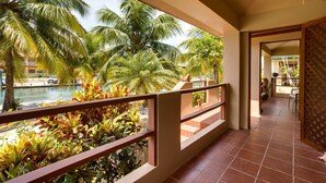 A balcony with a view of a pool and palm trees, a tiled floor, and a wooden railing. - Beautiful Island Townhome Overlooking Caribbean (Placencia Village)