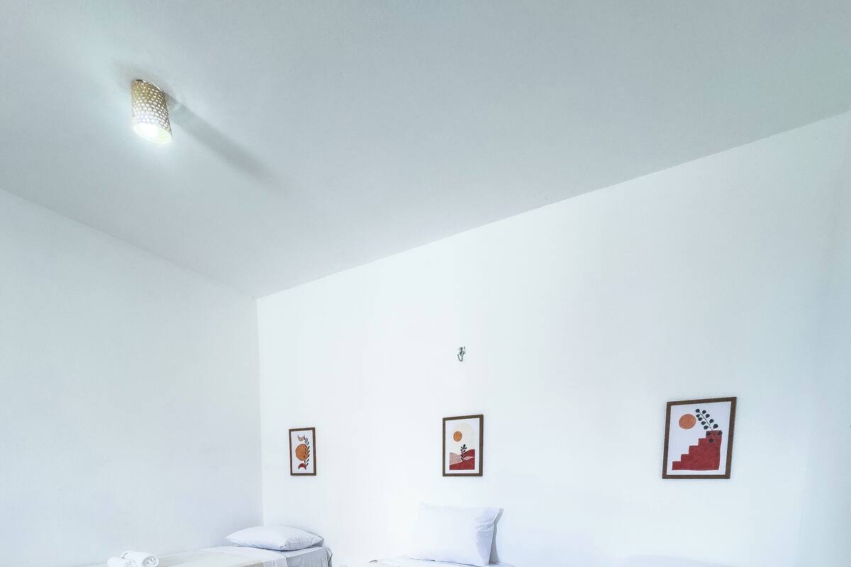 A hotel room with two single beds, a small table, and a wall-mounted light fixture.