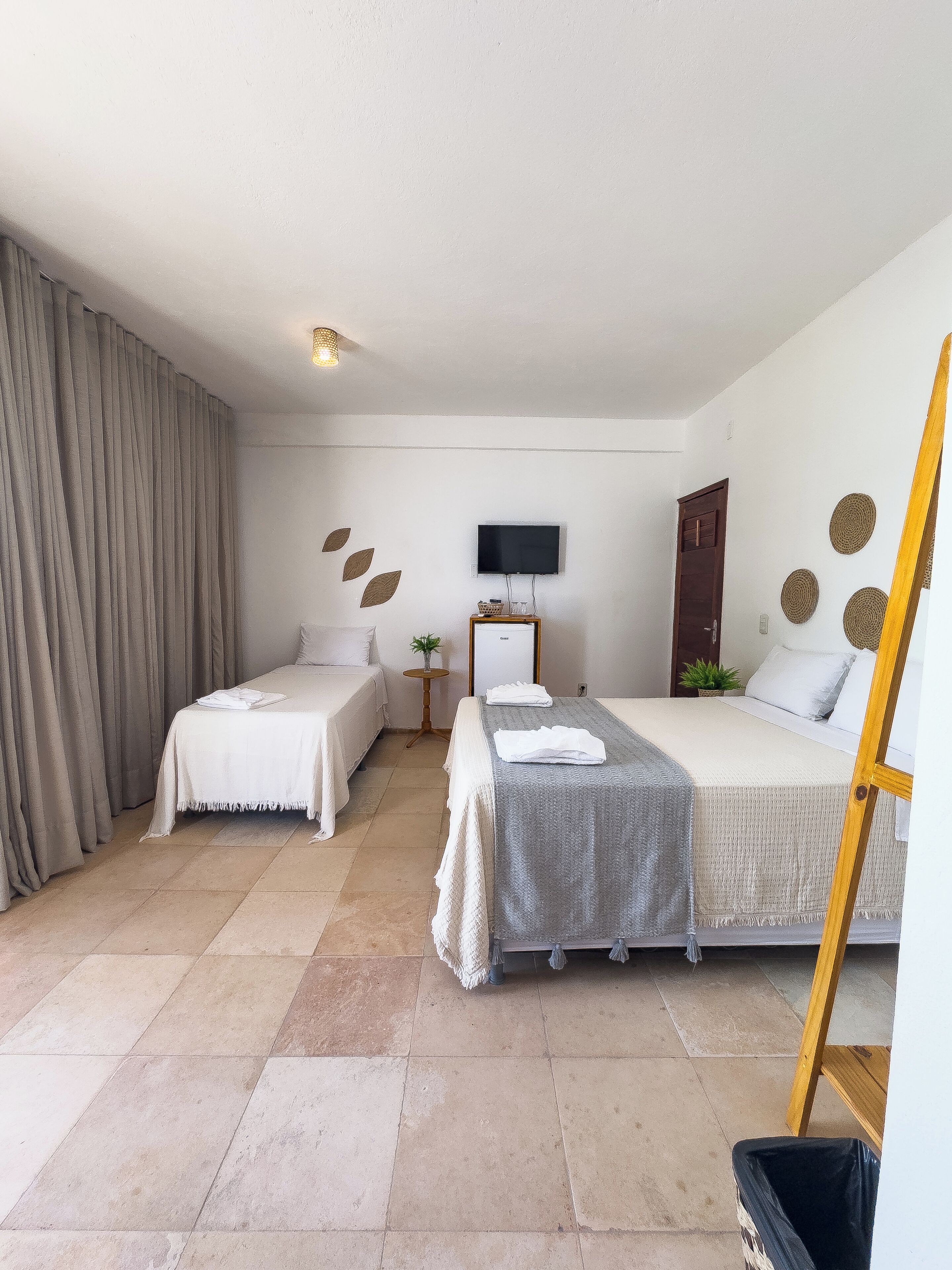 A hotel room with two beds, a TV, a small table with a plant, and a wooden chair.