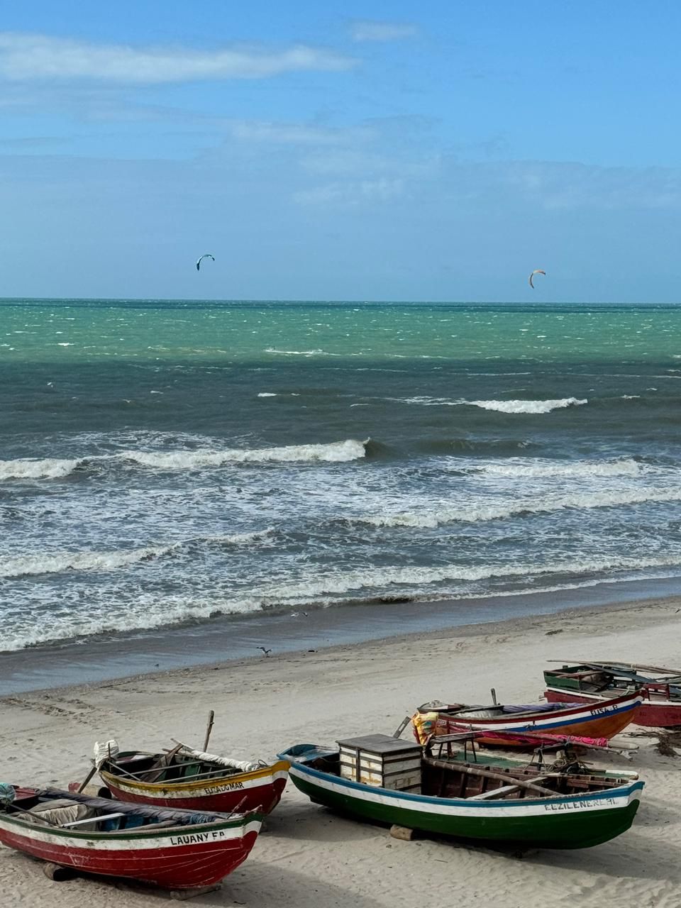 Een strand met diverse boten op een rij in het zand en de oceaan op de achtergrond.
