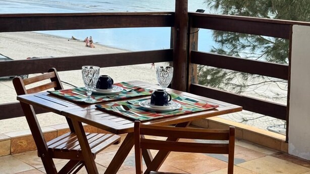 Ένα ξύλινο τραπέζι με δύο καρέκλες σε ένα μπαλκόνι με θέα στην παραλία.