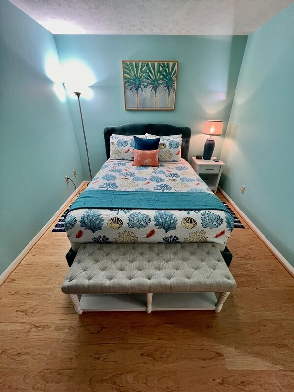 Un dormitorio con cama, mesita de noche, lámpara y un cuadro en la pared.