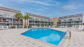 Una piscina con solárium de baldosas, rodeada de edificios de varios pisos con balcones y un cielo azul despejado.