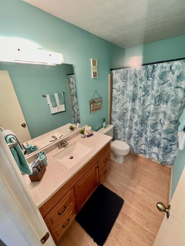 Baño con lavamanos, espejo e inodoro. Hay una cortina de ducha con estampado de hojas.