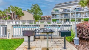 Un patio con una parrilla, una mesa y sillas, rodeado por una cerca blanca y una piscina.