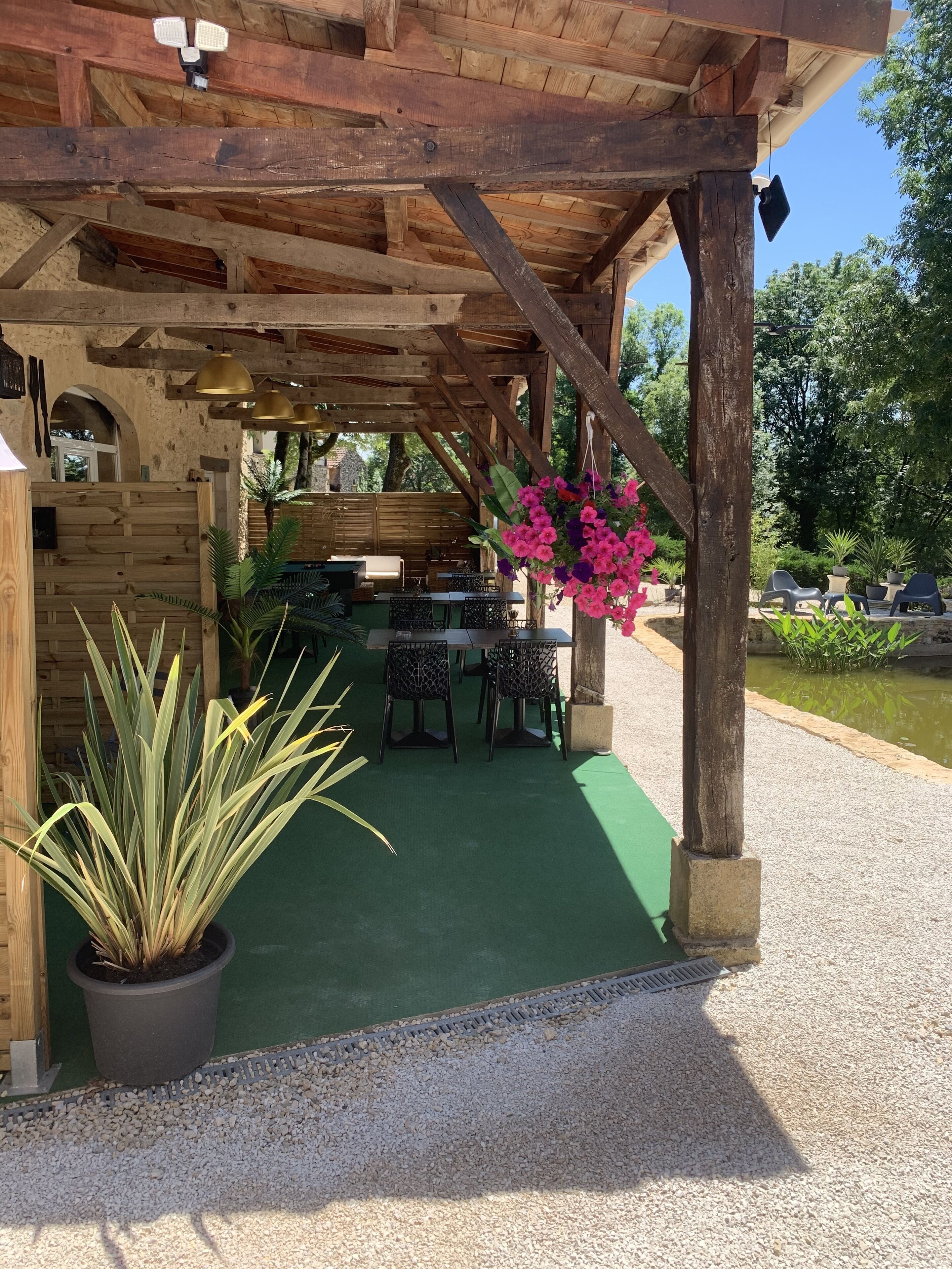 Zona relax all'aperto riparata, con travi in legno, pavimento verde e un tavolo con sedie.