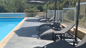 A poolside area with lounge chairs and umbrellas, a pool, and a view of trees and a fence. - La biche au bois  (Montclera)