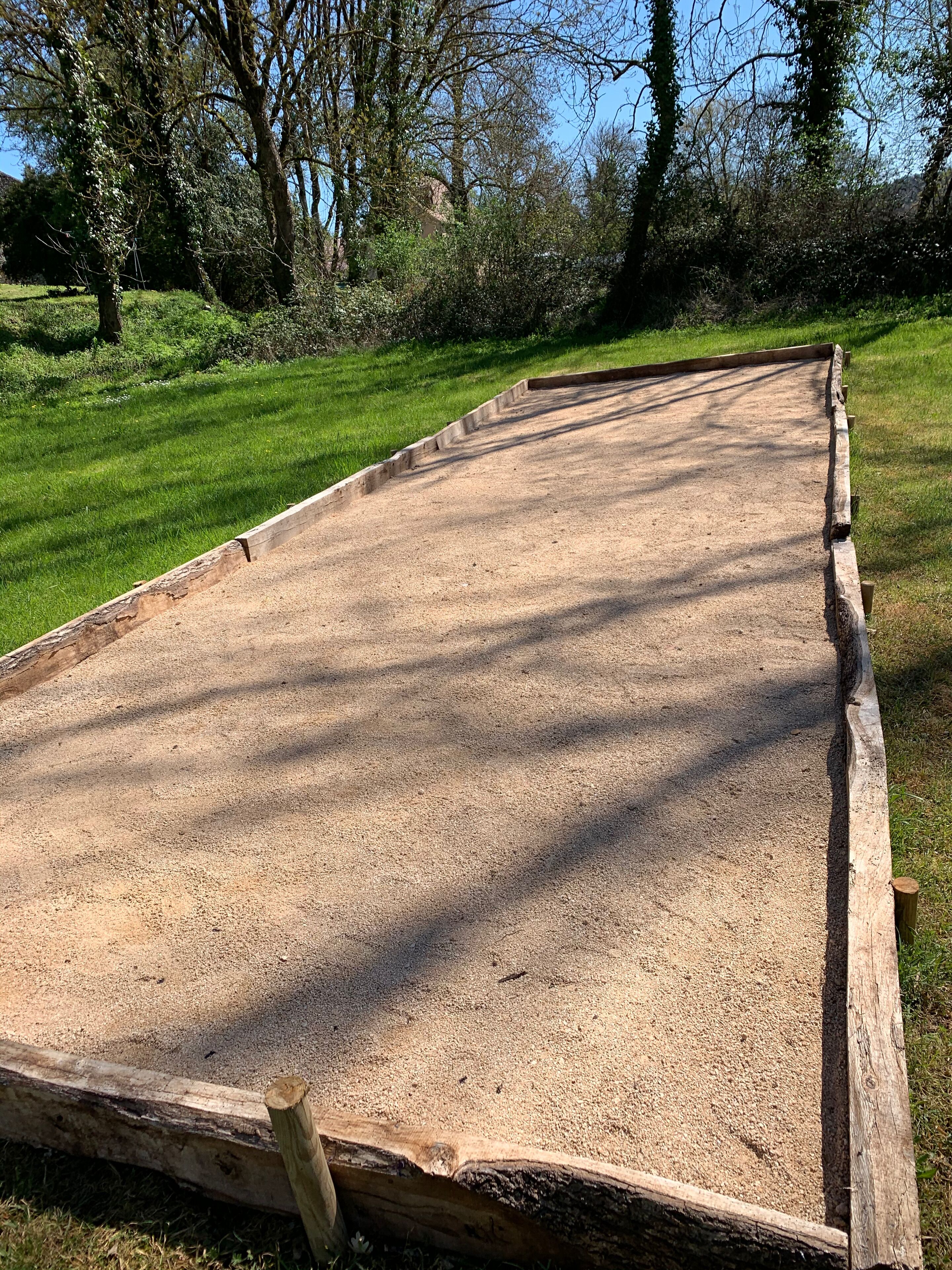 A long, narrow wooden structure with a gravel surface, surrounded by grass and trees.