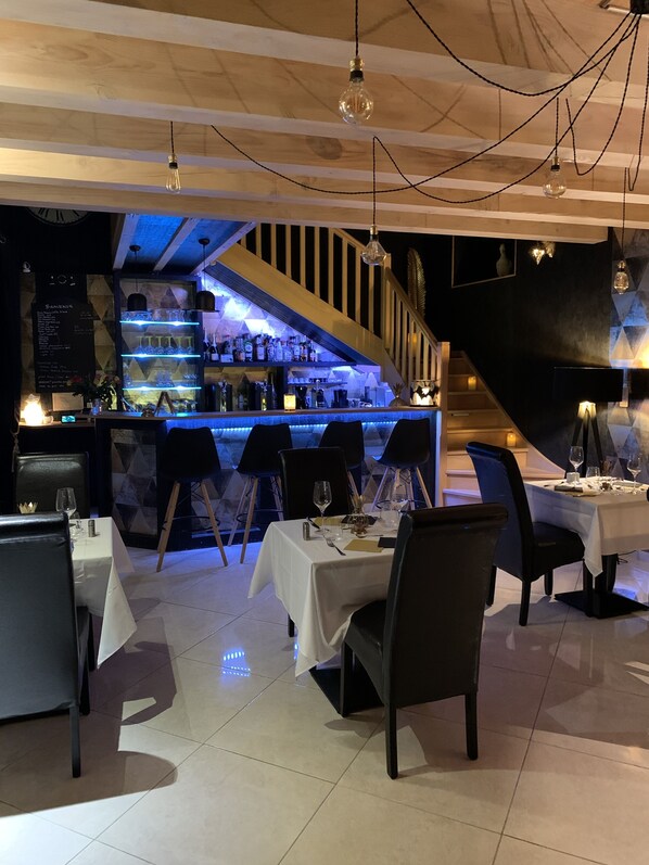 Un restaurante con zona de bar, varias mesas y sillas.