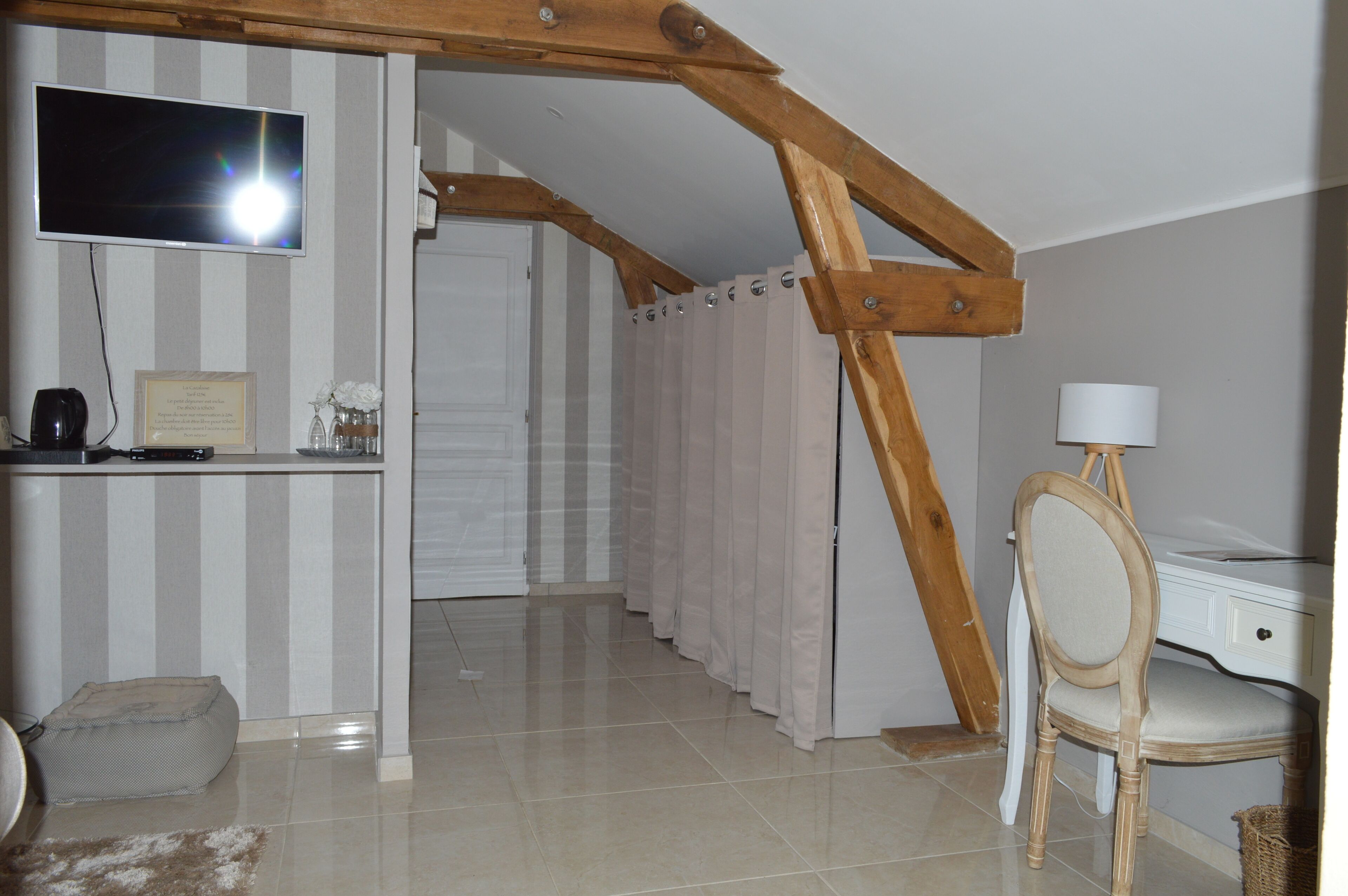 Une pièce avec un téléviseur fixé au mur, un bureau avec une lampe, une chaise et un lit avec un rideau à rayures.