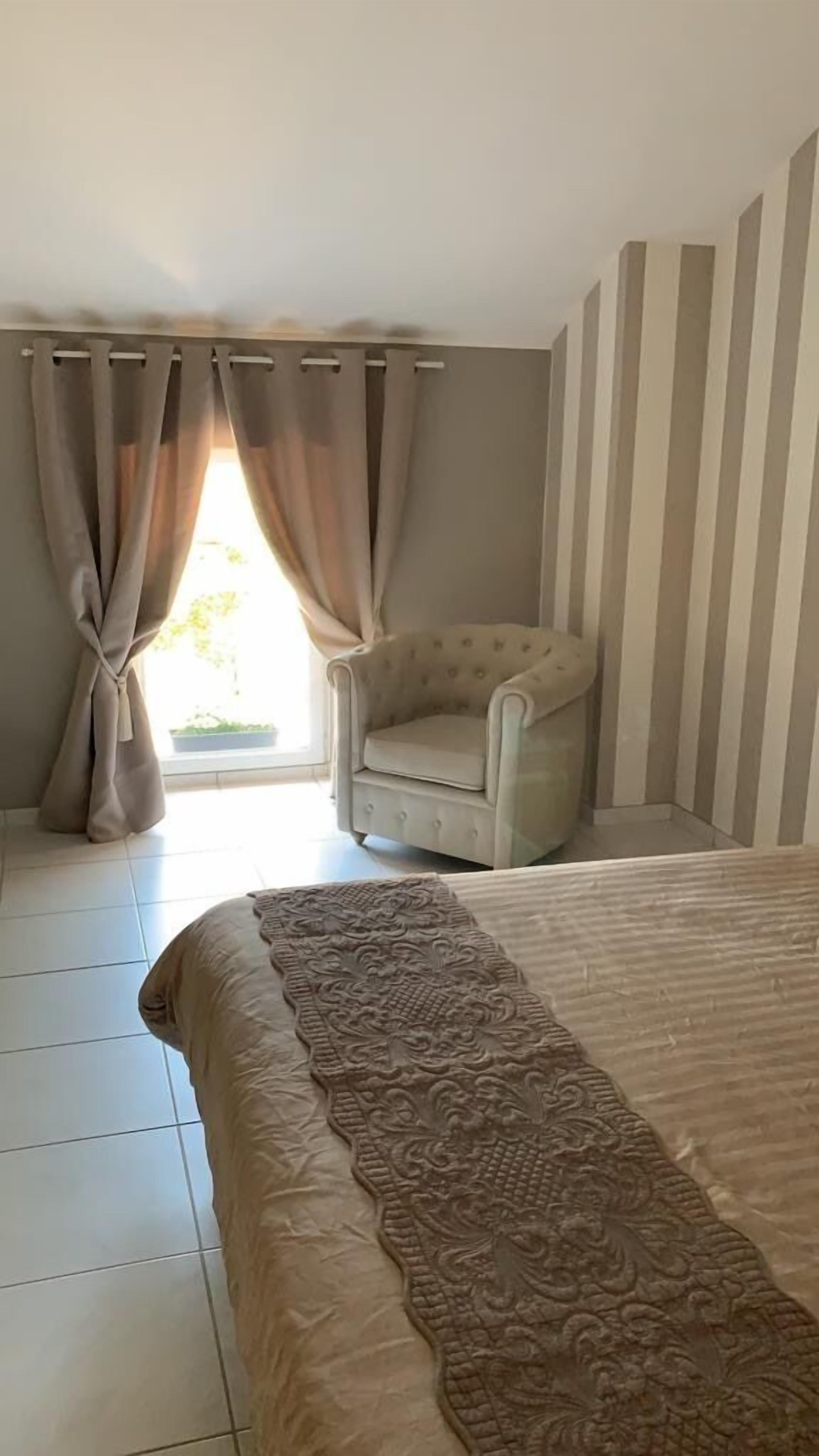A bedroom with a bed, a chair, curtains, and a window.