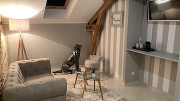 Una habitación acogedora con un sillón capitonado, una mesita de vidrio con una planta pequeña, una escultura de madera, una pared a rayas y un televisor montado.