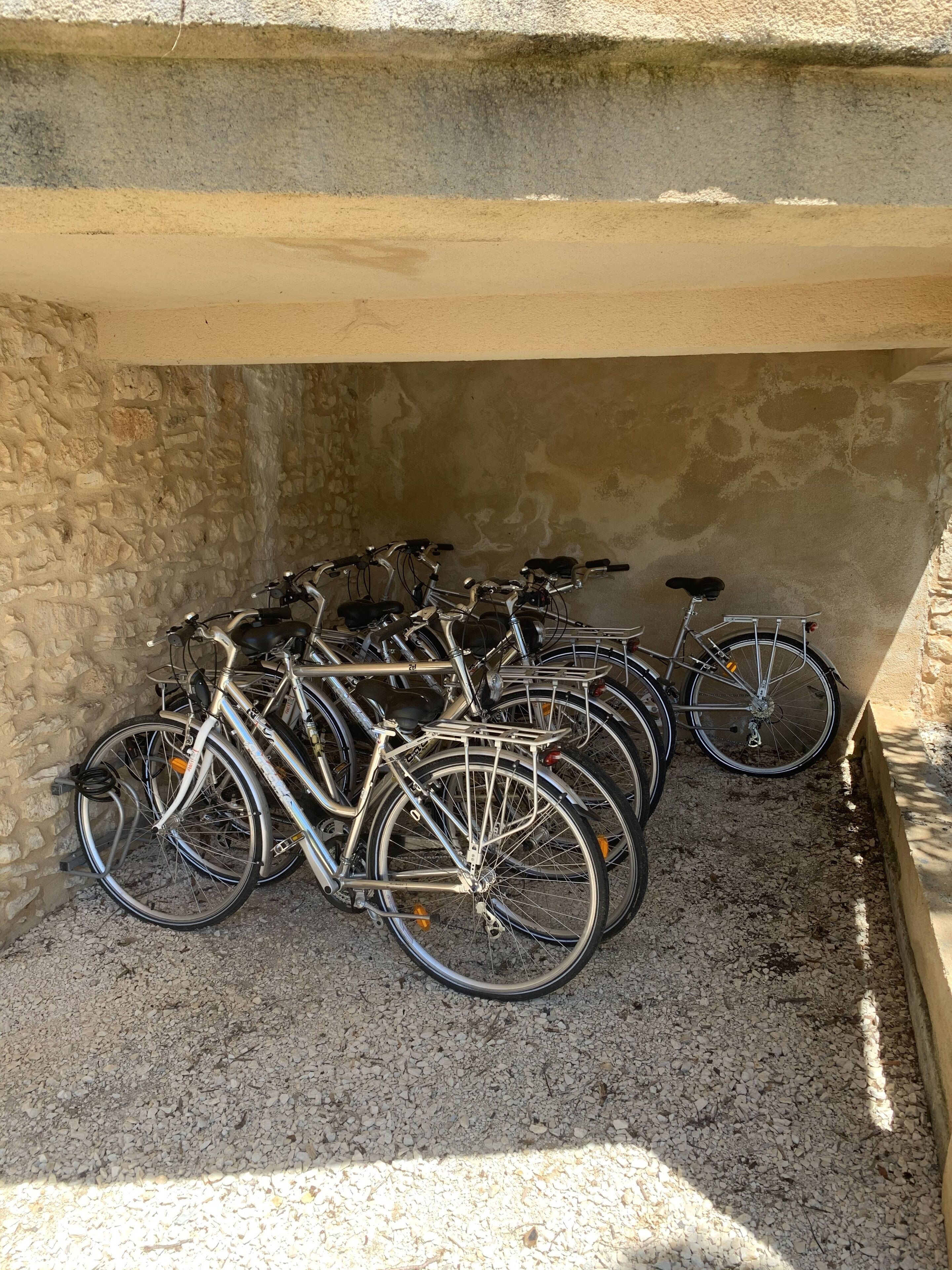 Varias bicicletas estacionadas junto a un muro de piedra en un espacio cubierto.