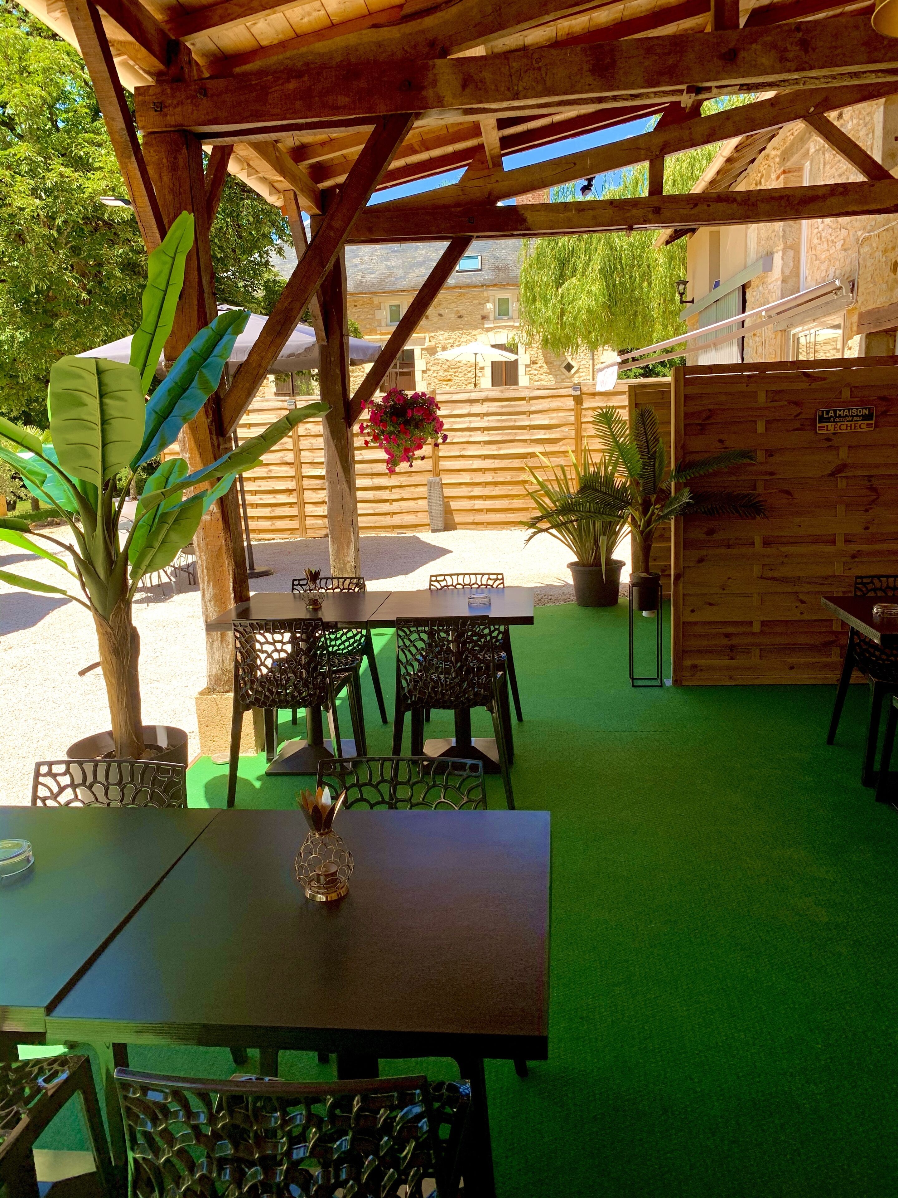 Une terrasse extérieure avec des tables et des chaises en bois, entourée d’une clôture en bois et agrémentée de plantes en pot.