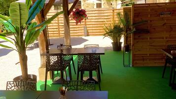 Une terrasse extérieure avec des tables et des chaises en bois, entourée d’une clôture en bois et agrémentée de plantes en pot.