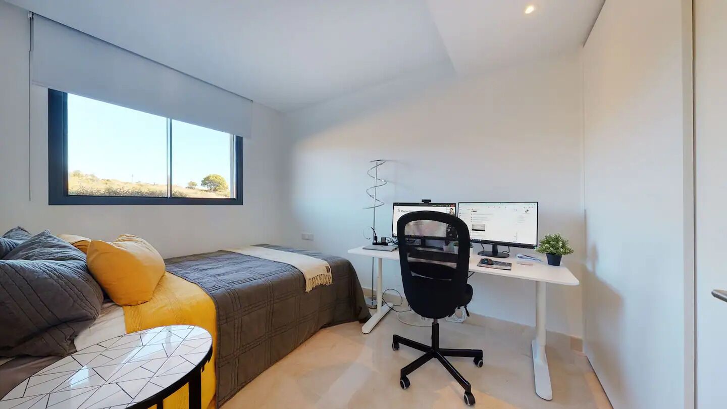 Une chambre avec un lit, un bureau avec un ordinateur et une fenêtre.