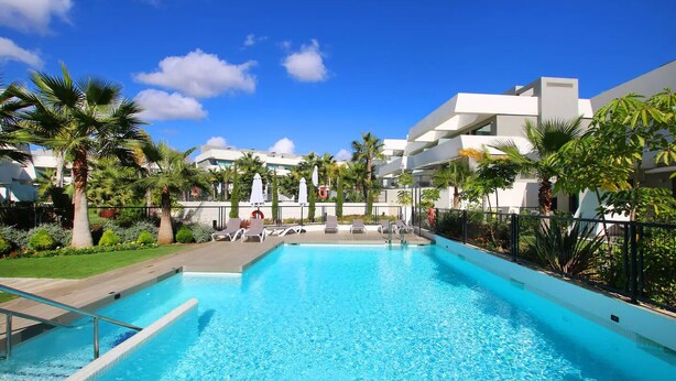 A swimming pool with lounge chairs and umbrellas, surrounded by palm trees and modern buildings. - Elegant La Cala Escape: Relax in Style in this Luxury Townhouse (La Cala de Mijas)